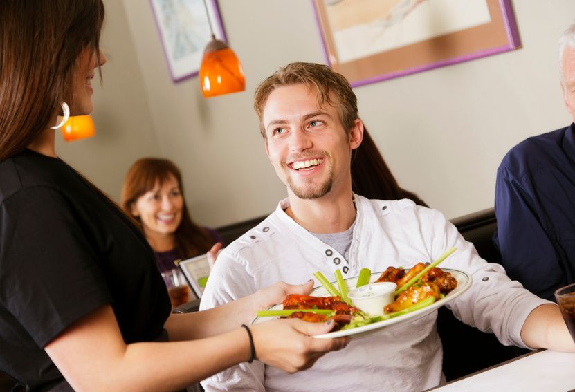 Mesero sirviendo un platillo a una mesa de clientes sonrientes